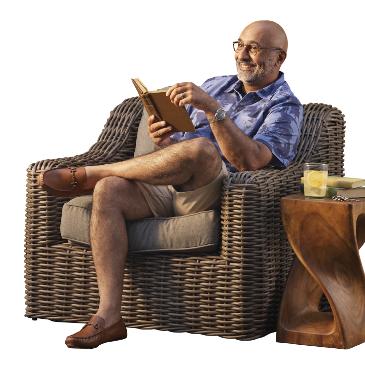 older well to do man smiling holding a book on his resort home patio
